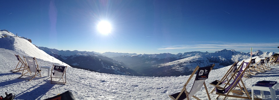 Vue sur une vallée enneigée en montagne avec le soleil et le ciel bleu en fond